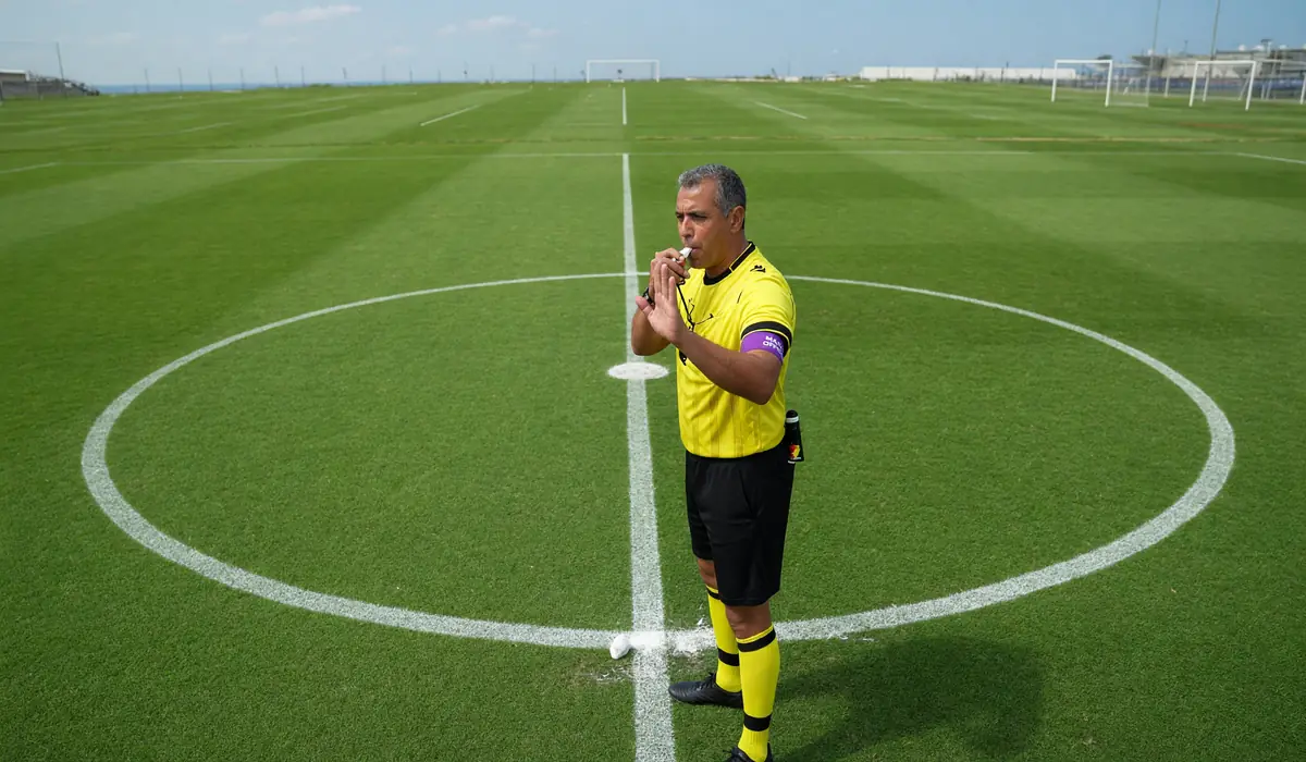 Football referee blowing whistle at center circle