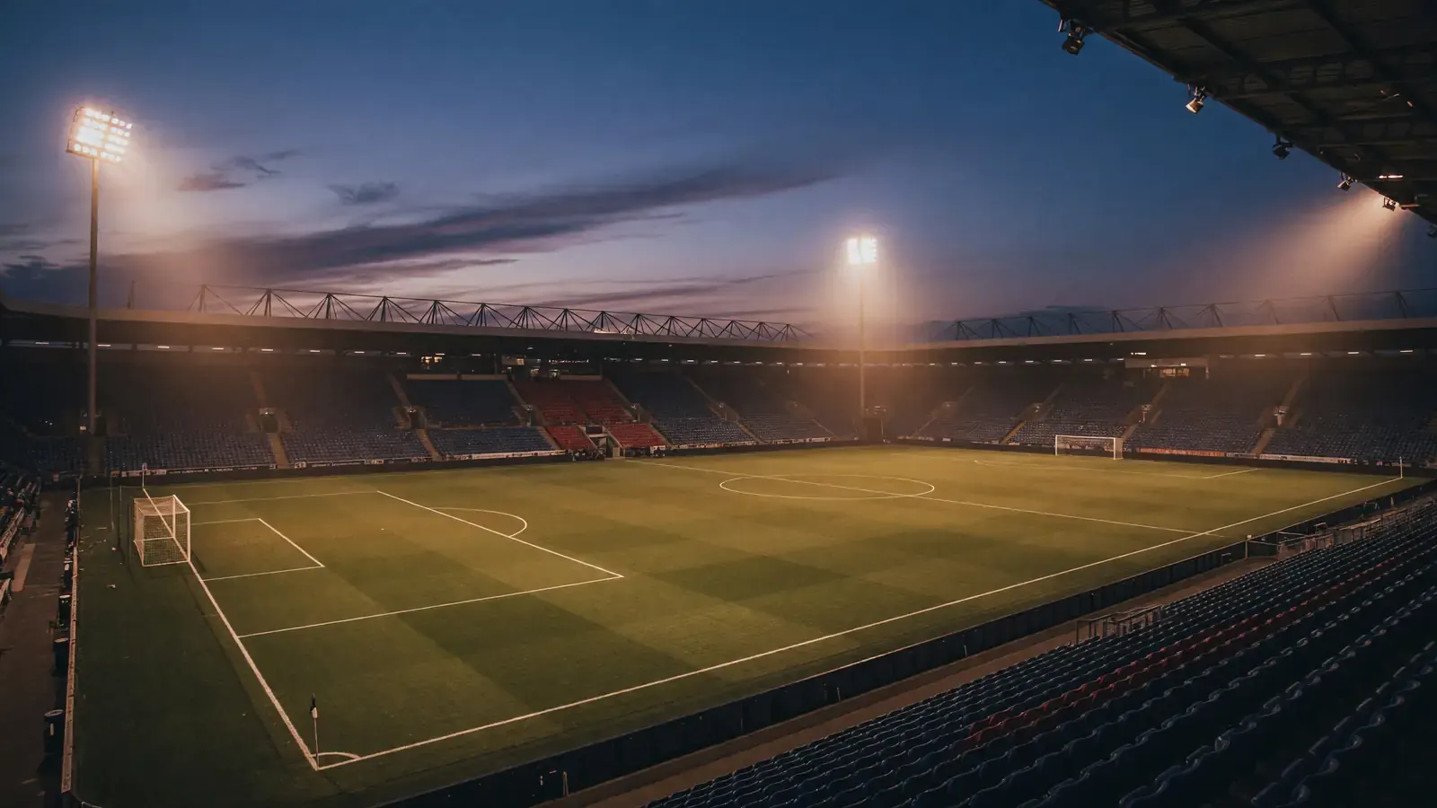 European football stadium at dusk with soft amber floodlights against a deep blue evening sky